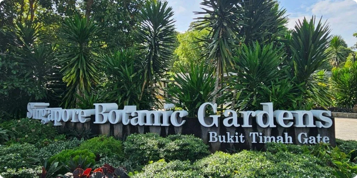 Entrance sign of Singapore Botanic Gardens positioned before a towering tree, welcoming visitors to the gardens.