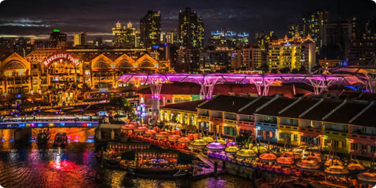 Nighttime cityscape of Clarke Quay, Singapore, showcasing vibrant lights and reflections on the water.