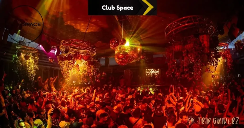 A large crowd dancing under disco balls and colorful lights at Club Space
