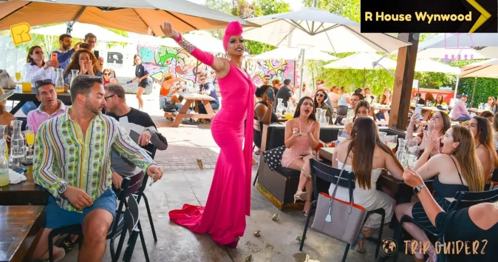 At R House Wynwood nightclub in Miami, a woman in a pink dress addresses a gathering of people at an outdoor event