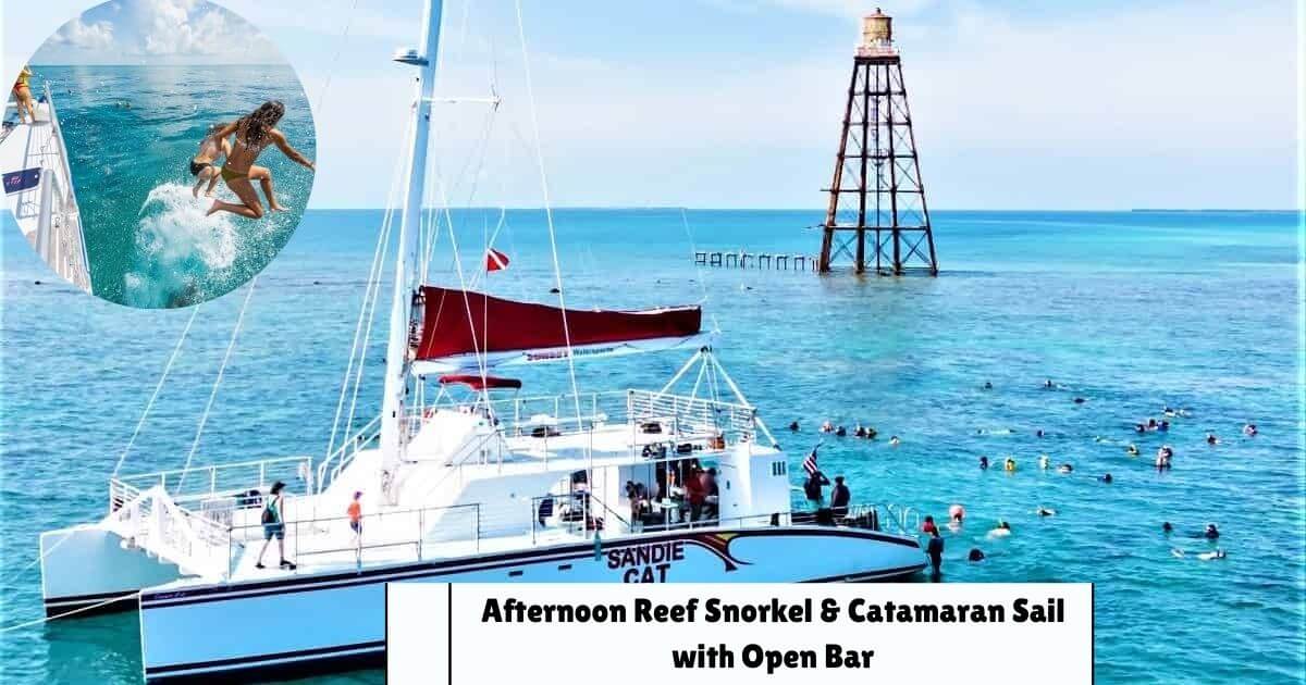A large catamaran boat with people snorkeling in the clear blue water near a lighthouse during a reef snorkel and sail excursion.
