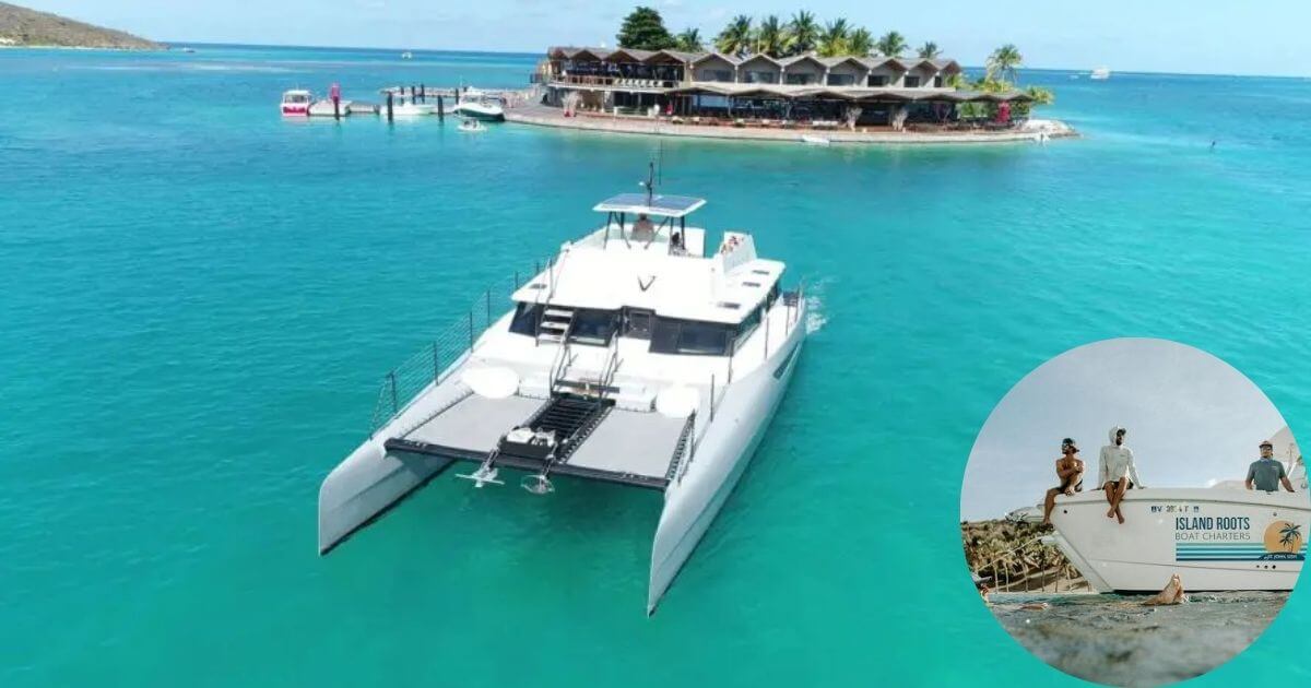 A large white catamaran boat sailing in the clear blue waters of the Caribbean, with a small island and buildings in the background. An inset shows two people relaxing on the bow of a different boat named "Island Roots."