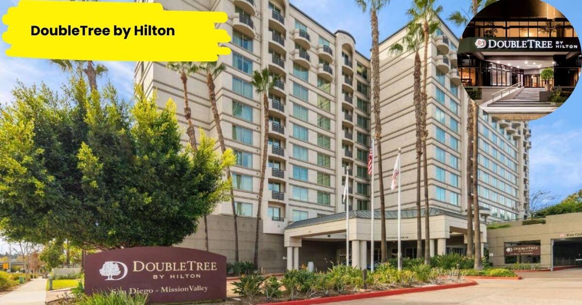 The front entrance of the DoubleTree by Hilton hotel in San Diego - Mission Valley. The multi-story modern building is surrounded by tall palm trees and lush greenery, with a prominent hotel sign visible at the front.