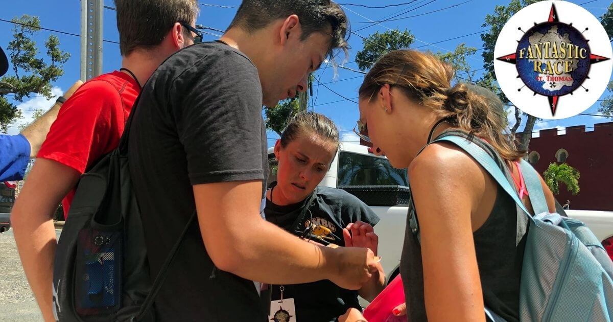 A group of people huddling together to look at a map during the "Fantastic St. Thomas Race" event. The race logo is visible in the top right corner.