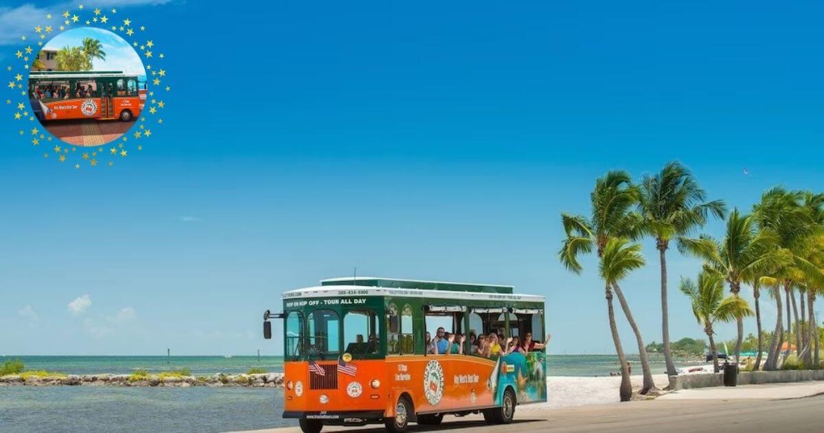 A vibrant orange and green open-air bus, a Conch Tour Train, driving along the coast next to palm trees on a sunny day.