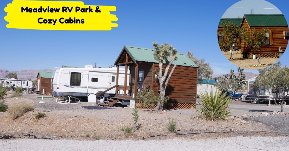 A photo of small, brown wood cabins with green roofs at Meadview RV Park & Cozy Cabins, surrounded by desert landscape and an RV. The clear blue sky and mountains are visible in the background.