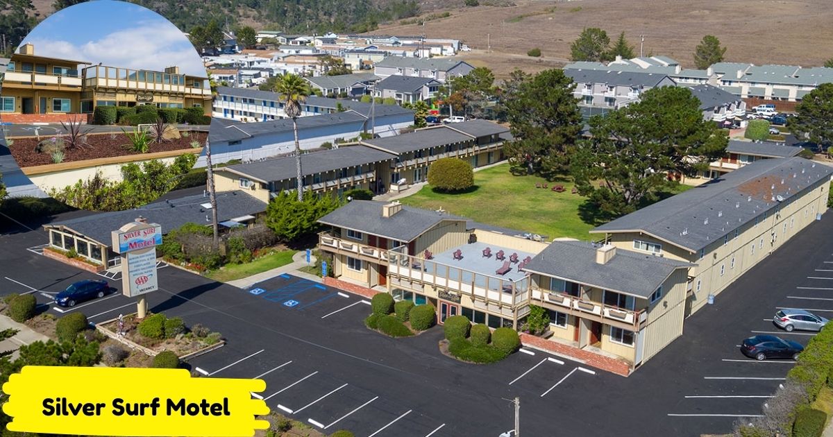 An aerial view of the Silver Surf Motel, a sprawling complex of one and two-story buildings with beige siding and brown roofs, surrounded by well-maintained green lawns and a parking lot.