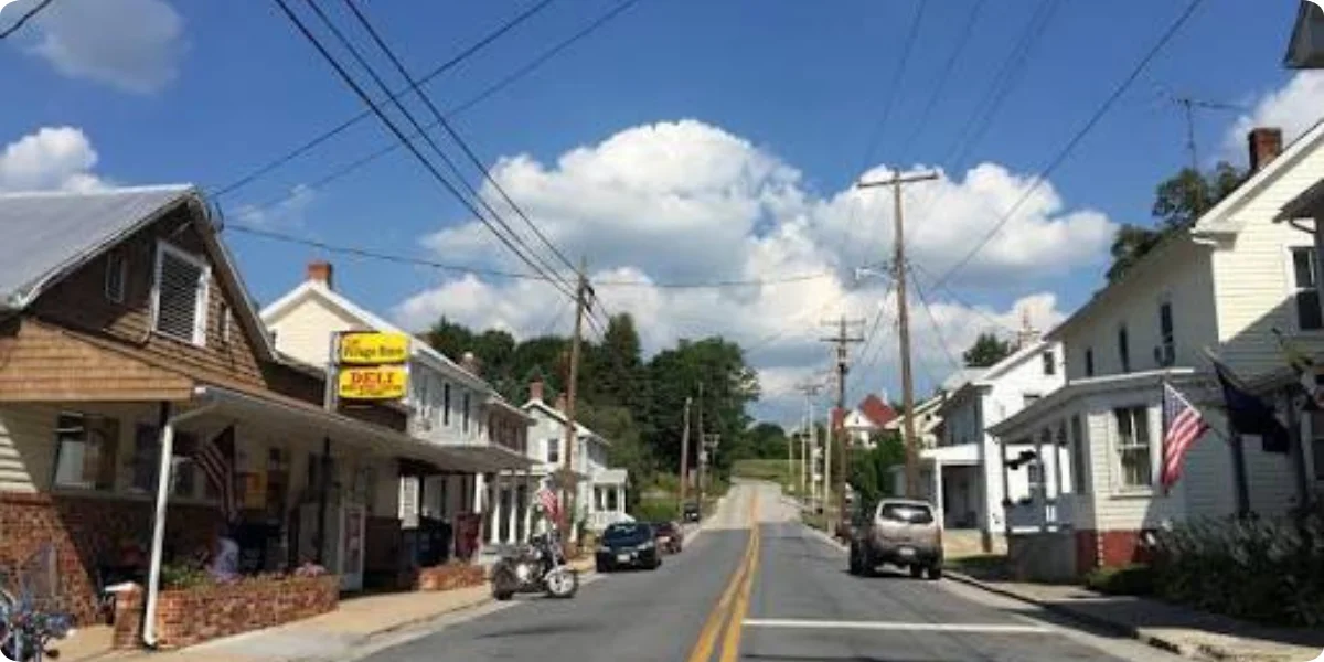 A small town street scene featuring a parked motorcycle alongside quaint shops and trees lining the road.