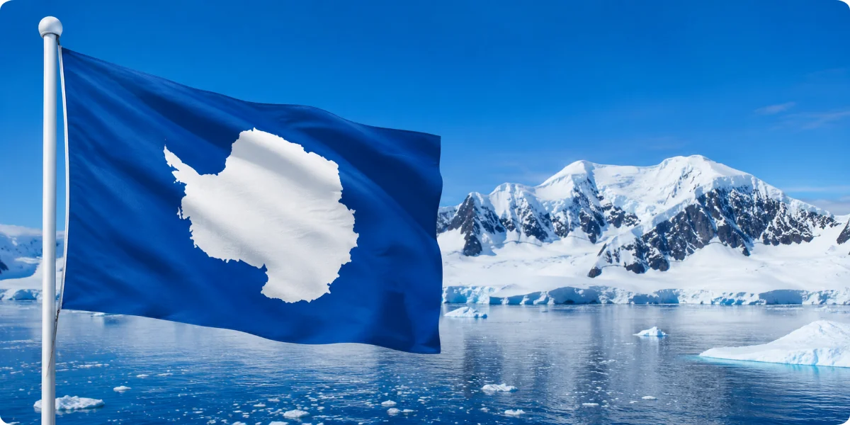 Flag of Antarctica displayed against a backdrop of icebergs and a clear blue sky.