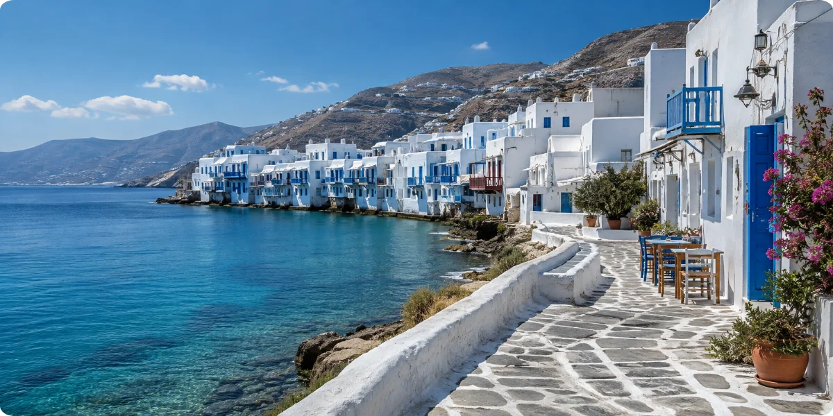 A serene coastal walkway in Mykonos, Greece, lined with smooth stones and overlooking calm blue waters.