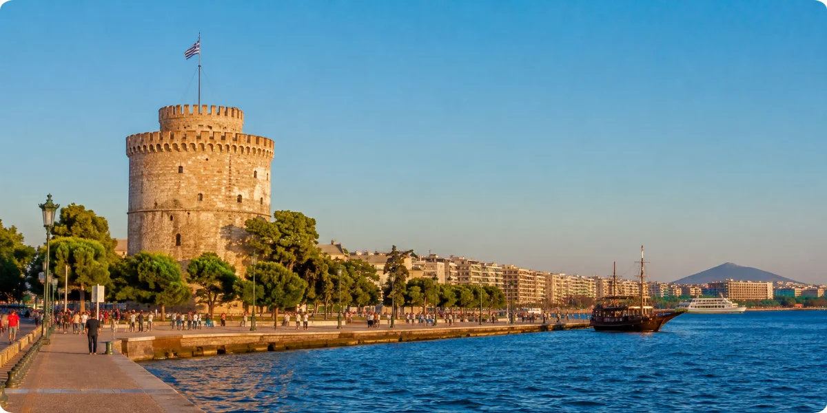 A boat is docked beside a tall tower in Thessaloniki, showcasing the city's waterfront and architectural features.