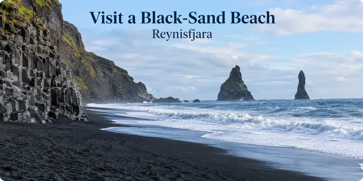 A scenic view of a black sand beach in Reykjavik, with waves gently crashing against the shore and rocky cliffs in the background.