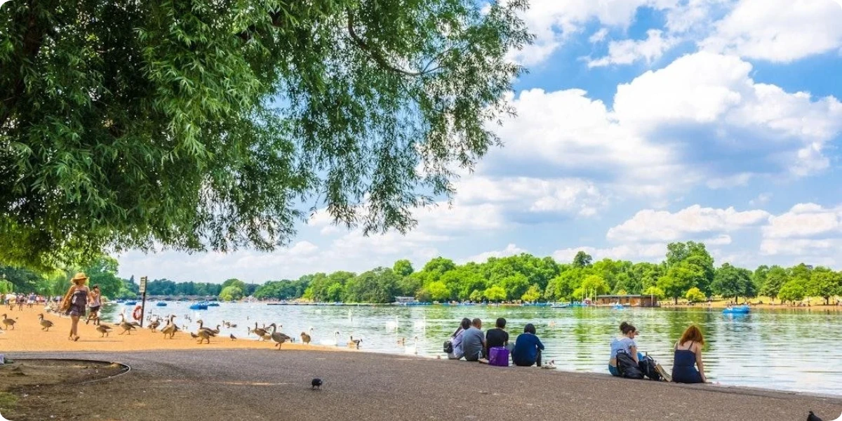Families enjoying the green lawns and Serpentine lake in Hyde Park, London.